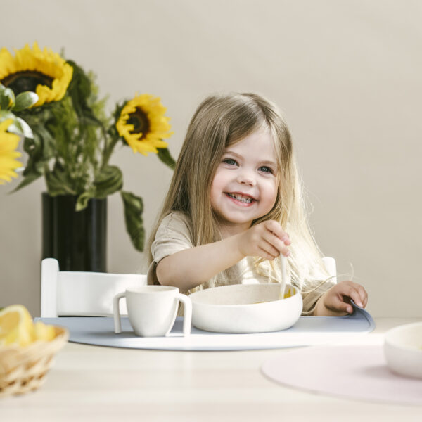 A blond girl sitting in table and eating from Skandino's tablewares.