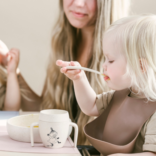 A photo of an article: What is the ideal spoon for a small child? A little girl eating solid from Skandino's tableware with Little My